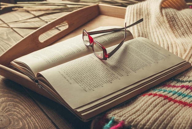 Books and glasses on wooden tray with knitted scarf ,close up