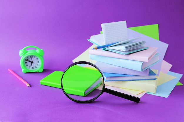 Books magnifying glass alarm clock and notepads pastel colored
paper purple background