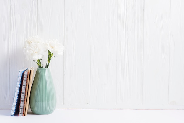 Foto i libri si avvicinano ai fiori freschi nel vaso contro la carta da parati bianca di legno dipinta