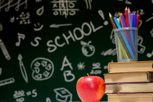 books, pencils and apple on table.