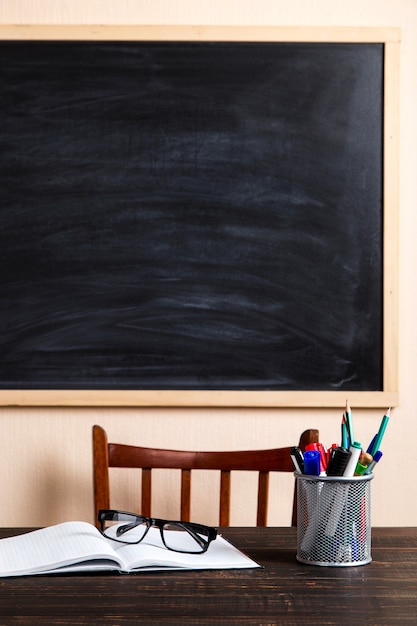 Photo books, pens, pencils and glasses on a wooden table, against a chalk board.