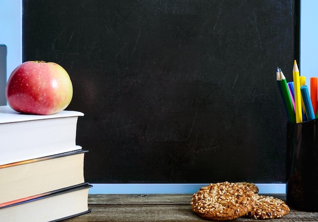 Libri forniture scolastiche biscotti integrali mela sul tavolo in classe davanti alla lavagna copia spazio