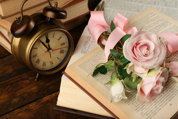 Books with flowers and clock on wooden background