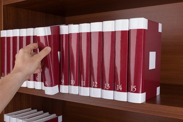 On the bookshelf man removes book. In the library.