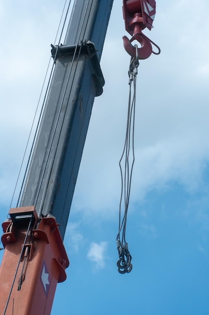 Boom of a tower crane in closeup against the blue sky A working crane on a construction site View of the crane hook cables and other hydraulic components and devices of construction machinery