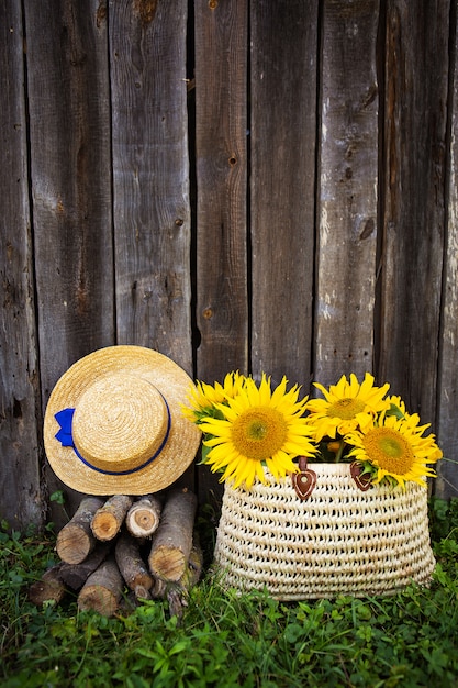 Boomstammen, een hoed, een boeket zonnebloemen in een strozak staan bij een houten huis