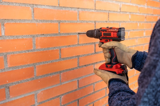 Boormachine met batterij die gaten maakt in een bakstenen muur buiten