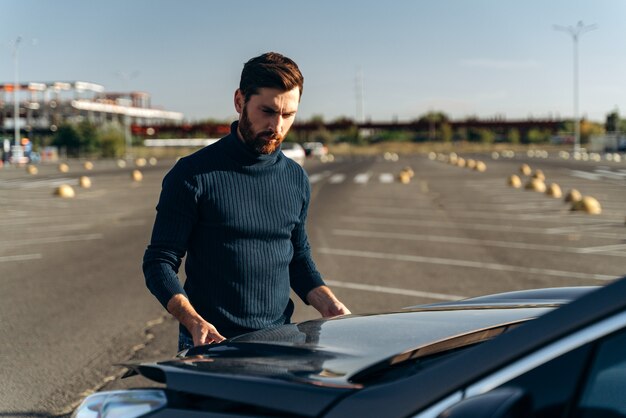 Boos bebaarde man die de motor van zijn auto controleert nadat hij op de weg kapot is gegaan. Serieuze man staat voor de kap. vervoersconcept: