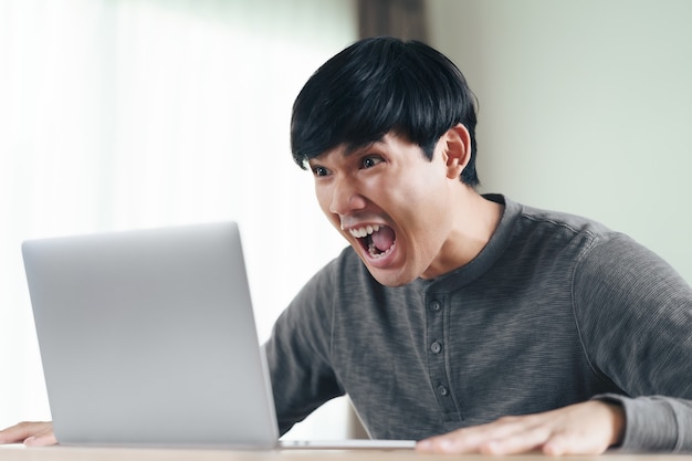 Boos geschokt verrast Aziatische man kijken naar laptop computerscherm zittend in de woonkamer.