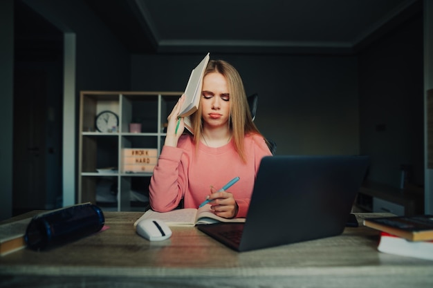 Boos grappige vrouw met een boek op haar hoofd studeert thuis met een laptop schrijft