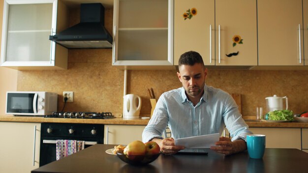 Boos jonge man leest brief met onbetaalde rekening in de keuken thuis