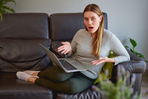 Boos jonge mooie vrouw met behulp van een laptopcomputer op de bank