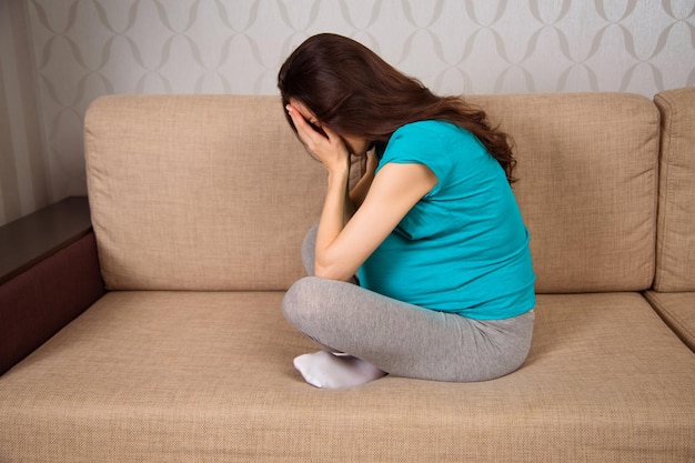 Boos jonge zwangere vrouw zittend op de bank thuis en huilt