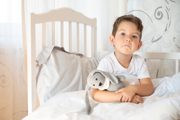 Boos jongen in bed in de ochtend. Eenzame peuter knuffelt een stuk speelgoed