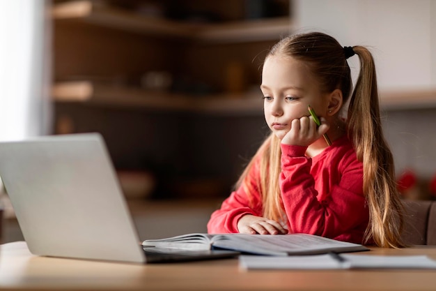 Boos klein schoolmeisje met boek en laptop moe van huiswerk