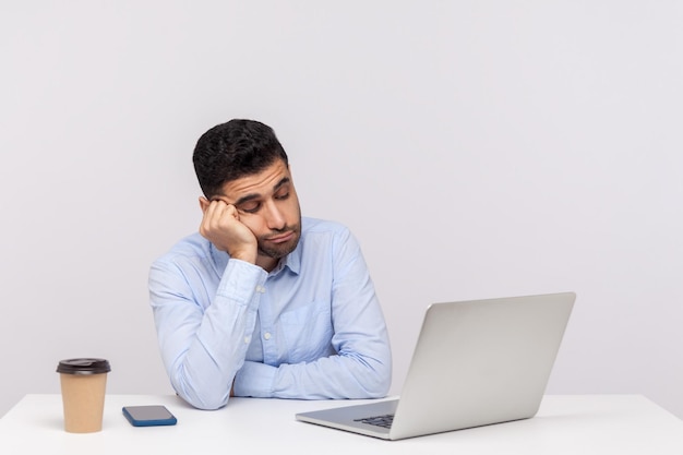 Boos luie inefficiënte man werknemer zit kantoor werkplek, kijken naar laptopscherm met onverschillige uitdrukking, vervelend online gesprek. indoor studio-opname geïsoleerd op een witte achtergrond