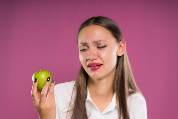 Boos meisje met een appel in handen op een roze achtergrond