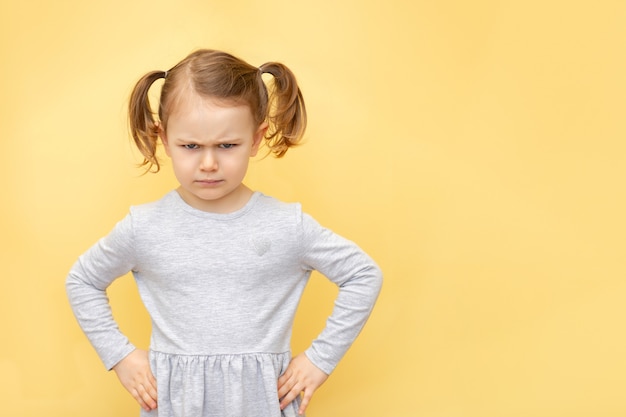 Boos schattig kind meisje met frustratie en meningsverschillen over pastel gele geïsoleerde muur