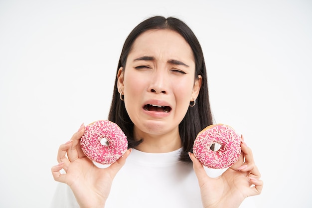 Boos snikkend meisje kan geen junkfood eten toont dat heerlijke geglazuurde donut witte achtergrond wil bijten