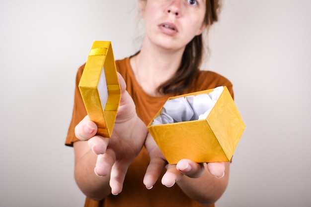 Boos vrouw, gekleed in bruine t-shirt met lege geschenkdoos geïsoleerd dan roze