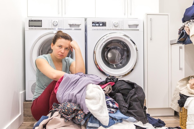 Boos vrouw in wasruimte zittend op een vloer met vuile kleren