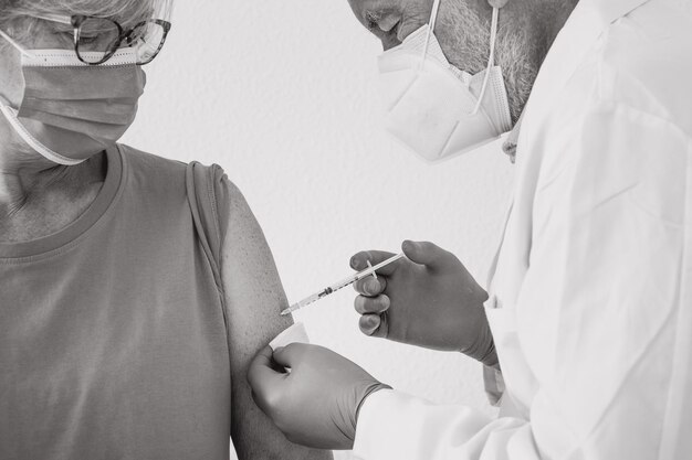 Booster coronavirus vaccine. Close-up of a doctor making  vaccination of Covid-19 to an elderly patient. Green pass concept