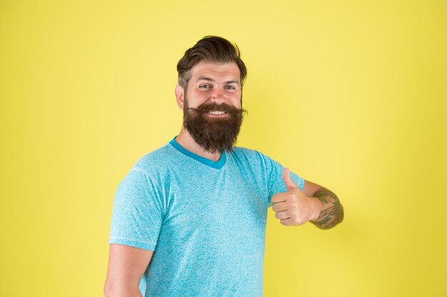 Boosting his mustache appeal Happy guy wearing beard and mustache on yellow background Bearded man smiling with stylish mustache shape Brutal hipster with textured mustache hair showing thumbs up