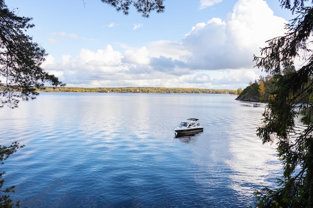 Foto boot op het blauwe meer onder de hemel met witte wolken en naaldbomen eromheen