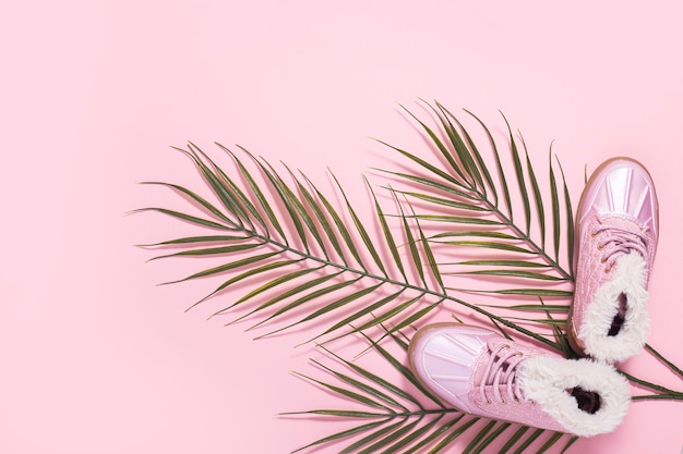 Boots for a girl, a leaf of a palm tree on a pink background. Top view, flat lay.