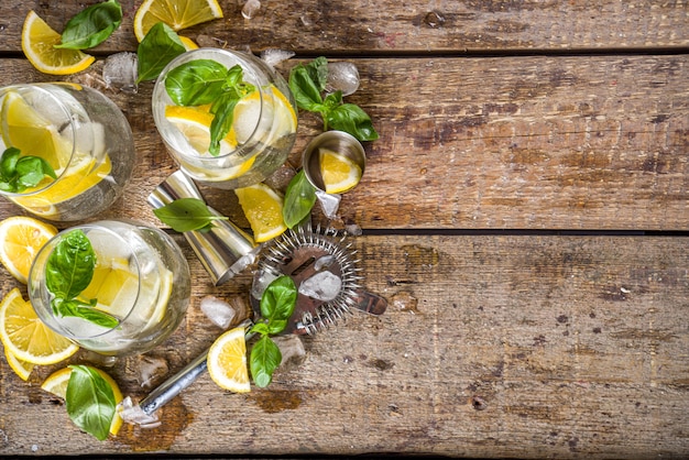 Boozy lemon basil lemonade, with fresh basil leaves, lemons and crushed ice, rustic wooden background copy space