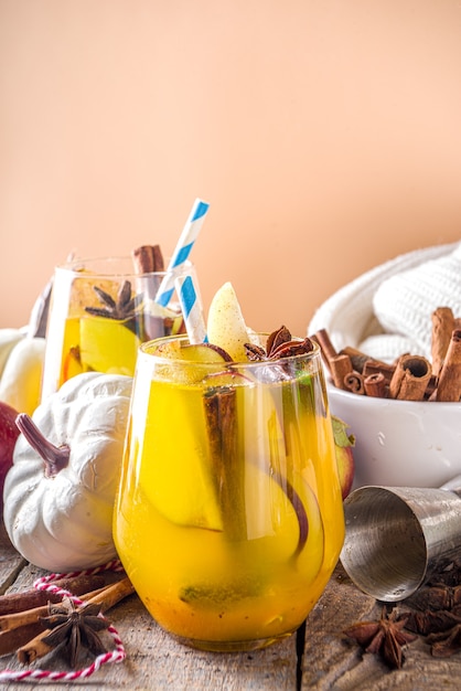 Boozy pumpkin party punch, thanksgiving sangria met pompoensap, appel, peer en kruiden, gezellige houten achtergrond met warme trui en ingrediënten kopieerruimte