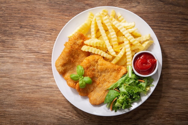 Bord gebakken gepaneerd kippenvlees of Schnitzel met frietjes en salade bovenaanzicht