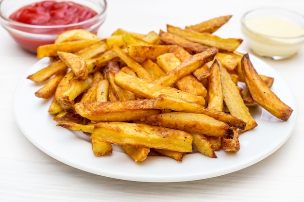 Bord met frietjes en schoteltjes met sauzen op de witte houten tafel