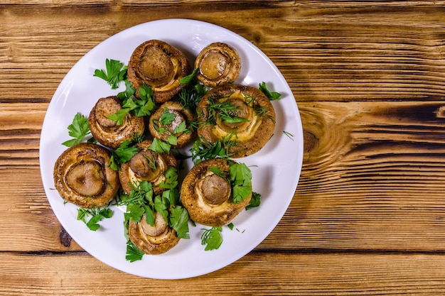 Bord met gebakken champignons, dille en peterselie op een houten tafel. Bovenaanzicht