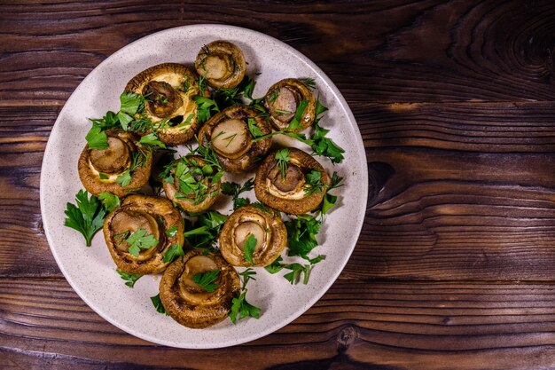 Bord met gebakken champignons, dille en peterselie op een houten tafel. Bovenaanzicht