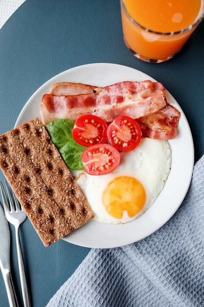 Bord met gebakken eieren, spek, tomaten, jus d'orange en toast.