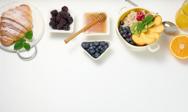 Bord met havermout en fruit, een halve rijpe sinaasappel en vers geperst sap in een transparante glazen karaf, honing in een kom op een witte tafel. Gezond ontbijt