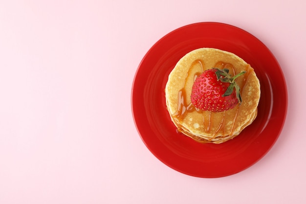 Bord met pannenkoeken met aardbei en karamel op roze achtergrond