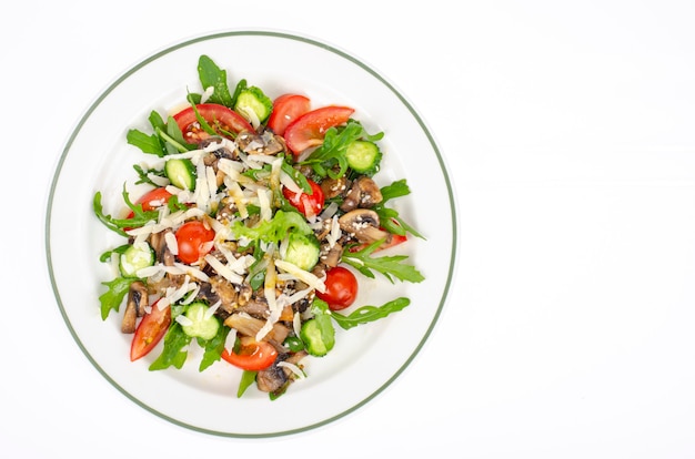 Bord met vegetarische schotel van rucola, tomaten en champignons op witte achtergrond.