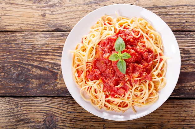 Bord pasta met tomatensaus en groene basilicum op houten tafel, bovenaanzicht