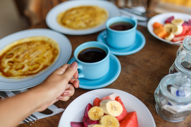 Borden met bananenpannenkoeken tropisch fruit en twee kopjes koffie op houten tafel