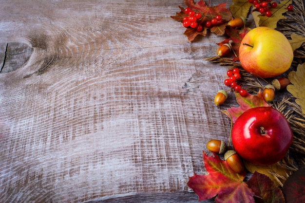 Confine di mele, bacche e foglie di autunno sul rustico in legno