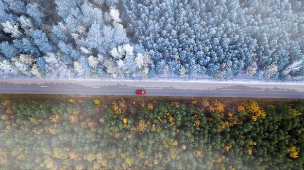 秋と冬の国境ドローンから見た森の頂上から車が道路を走る