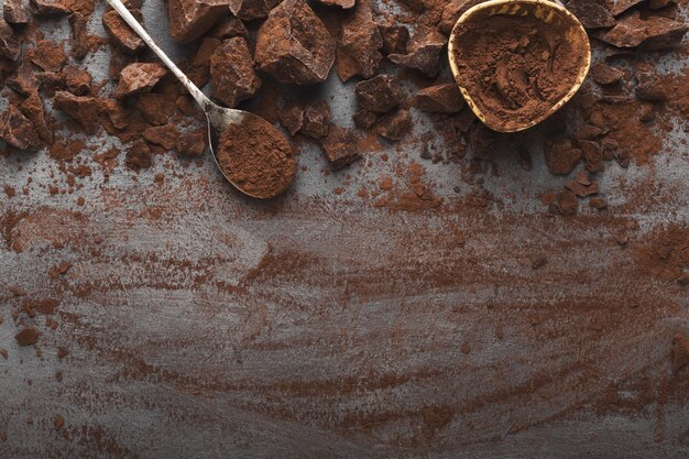 Border of chocolate chunks crushed on dark background and cocoa powder in bowl and spoon, top view, copy space. Confectionery shop advertising and cooking ingredients concept, mockup for recipe