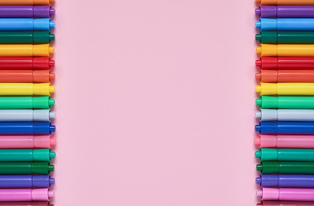 Border of colored felt tip pens on pink background with copyspace. Top view