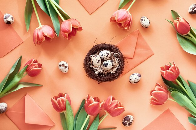 Border made from Spring tulips, quail eggs, greeting cards and envelopes with bird nest in the middle.