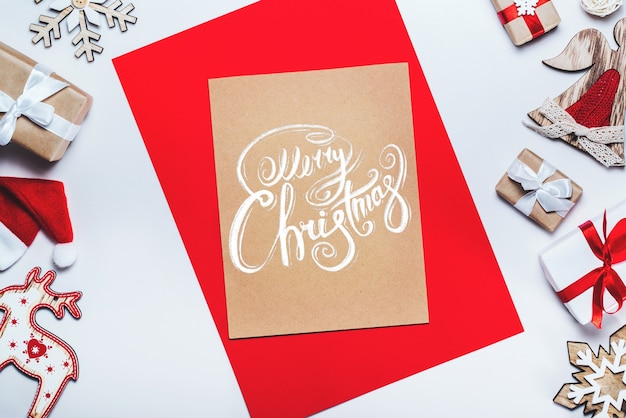 Photo border of new year decorations and gifts on white background with merry christmas wishes written with calligraphic font on craft paper piece