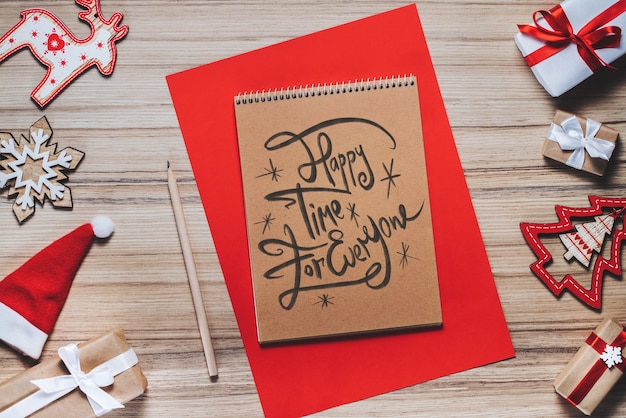 Photo border of new year decorations and gifts on wooden background with merry christmas wishes written with calligraphic font at the opened notebook