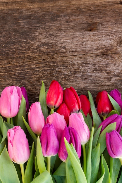 Border of red, pink and purple tulip flowers on wooden table