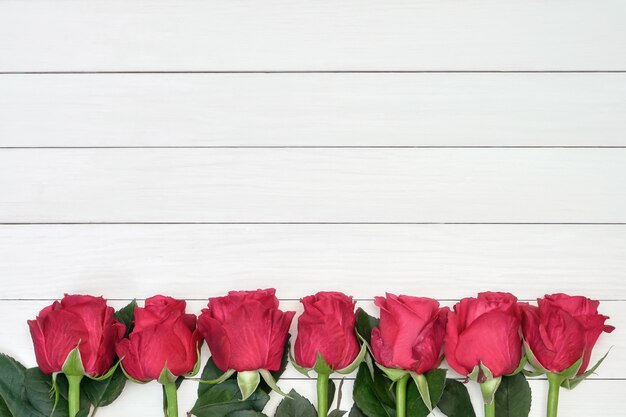 Border of red roses on white wooden background. Top view, copyspace.